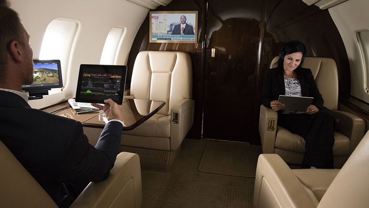 Man viewing stocks on iPad and woman watching tablet while cable news plays on TV in business jet cabin